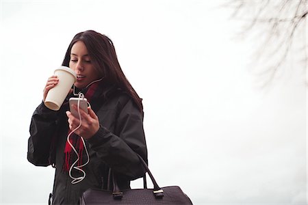 simsearch:614-06336113,k - Happy woman listening music on mobile while drinking coffee against sky Stock Photo - Premium Royalty-Free, Code: 6109-08953652