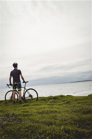 simsearch:6109-08928532,k - Athlete standing with his bicycle on grass near the sea Photographie de stock - Premium Libres de Droits, Code: 6109-08928444