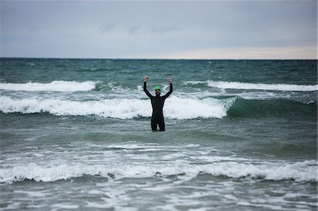 simsearch:400-03956564,k - Athlete in wet suit standing in the sea with raised hands Fotografie stock - Premium Royalty-Free, Codice: 6109-08928484