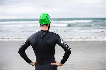 simsearch:400-03956564,k - Rear view of athlete in wet suit standing with his hands on his waist on the beach Fotografie stock - Premium Royalty-Free, Codice: 6109-08928485