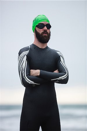 simsearch:6109-08928446,k - Athlete in wet suit standing with his hands crossed on the beach Photographie de stock - Premium Libres de Droits, Code: 6109-08928494