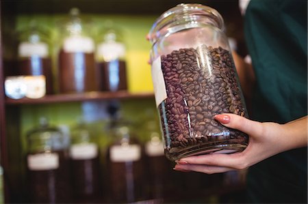 Mid section of female shopkeeper holding jar of coffee beans at counter in shop Stock Photo - Premium Royalty-Free, Code: 6109-08928581