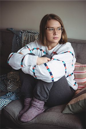 simsearch:6109-08944356,k - Thoughtful woman sitting and hugging her knees in living room at home Stock Photo - Premium Royalty-Free, Code: 6109-08928694