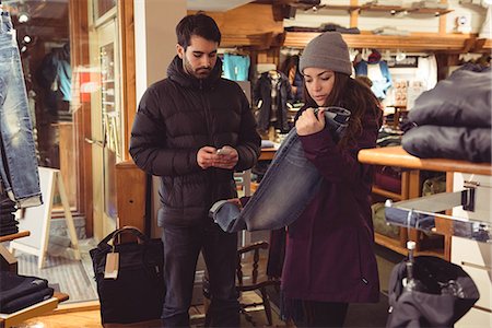 shopper texting - Woman selecting apparel in a clothes shop while man using mobile phone Stock Photo - Premium Royalty-Free, Code: 6109-08928881