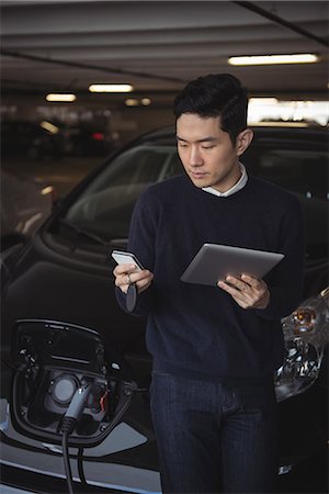 simsearch:700-07498125,k - Man using digital tablet and mobile phone while charging electric car in garage Stock Photo - Premium Royalty-Free, Code: 6109-08928988