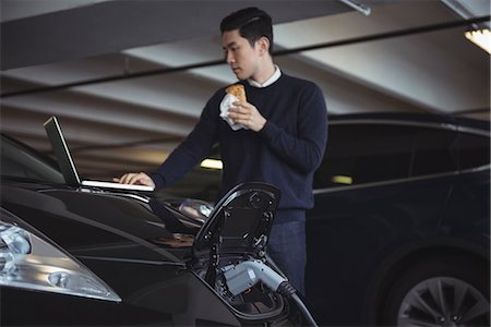 electric sockets - Man using laptop while charging electric car in garage Stock Photo - Premium Royalty-Free, Code: 6109-08928996