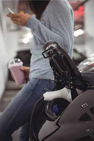 Car being charged with electric car charger while woman standing in background at electric vehicle charging station Stock Photo - Premium Royalty-Free, Code: 6109-08929065