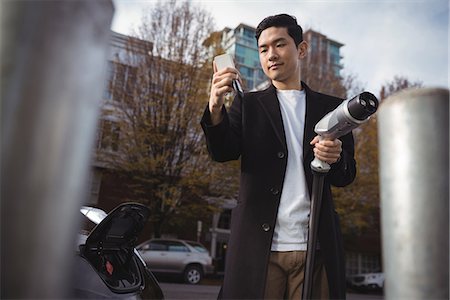 simsearch:6109-08929067,k - Man using mobile phone while holding car charger at electric vehicle charging station Fotografie stock - Premium Royalty-Free, Codice: 6109-08929075