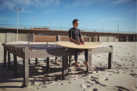 surfing extreme sport - Thoughtful surfer sitting on a wooden platform with surfboard on beach Foto de stock - Sin royalties Premium, Código: 6109-08929160