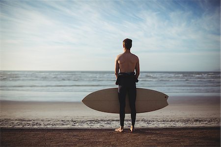 simsearch:649-07437735,k - Rear view of surfer standing with surfboard on beach Photographie de stock - Premium Libres de Droits, Code: 6109-08929201