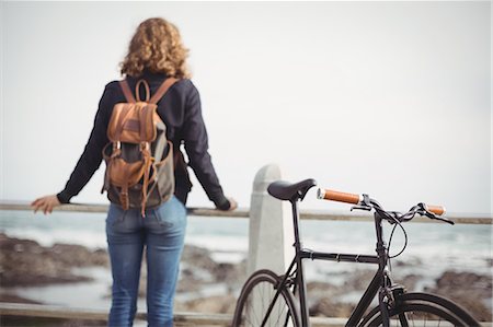 Rear-view of a woman standing with the bicycle near the seashore Stock Photo - Premium Royalty-Free, Code: 6109-08929234