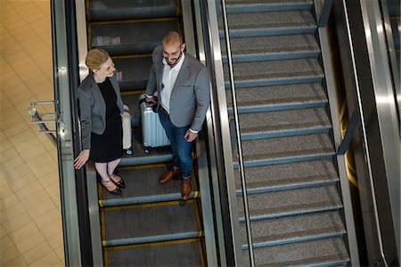 simsearch:628-05817505,k - Businesspeople interacting with each other while moving down on escalator at airport terminal Photographie de stock - Premium Libres de Droits, Code: 6109-08929358