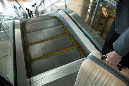 simsearch:6109-08929360,k - Businesswoman with luggage moving down on escalator at airport terminal Photographie de stock - Premium Libres de Droits, Code: 6109-08929359