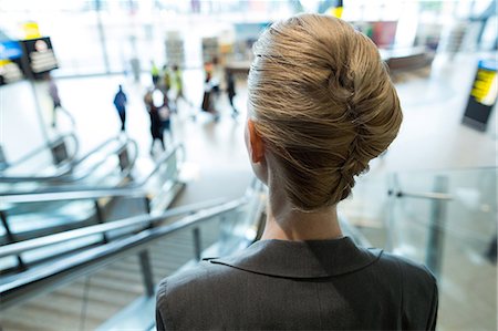 Rear view of businesswoman moving down on escalator at airport terminal Stock Photo - Premium Royalty-Free, Code: 6109-08929361