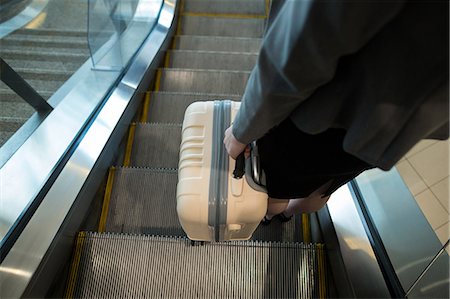 simsearch:6108-05859735,k - Businesswoman with luggage moving down on escalator at airport terminal Photographie de stock - Premium Libres de Droits, Code: 6109-08929362