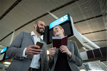 simsearch:6109-08802694,k - Business people holding boarding pass and using mobile phone in airport terminal Stock Photo - Premium Royalty-Free, Code: 6109-08929371