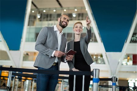 simsearch:632-08129867,k - Businesswoman standing with her colleague and pointing at the distance at airport terminal Stock Photo - Premium Royalty-Free, Code: 6109-08929380