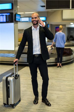 Businessman with luggage talking on mobile phone in waiting area in airport terminal Stock Photo - Premium Royalty-Free, Code: 6109-08929385