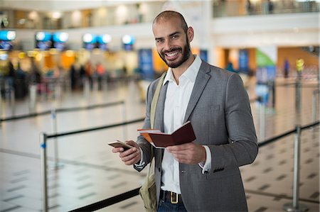 Smiling businessman holding a boarding pass and checking his mobile phone at airport terminal Stock Photo - Premium Royalty-Free, Code: 6109-08929399