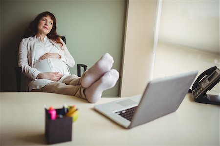 pregnant lady belly - Pregnant businesswoman relaxing with her feet up in office Foto de stock - Sin royalties Premium, Código: 6109-08929327