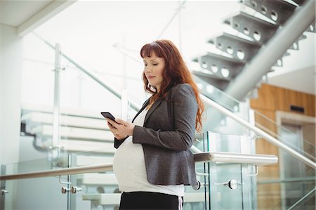 simsearch:6109-08953148,k - Pregnant businesswoman using mobile phone near staircase in office Stock Photo - Premium Royalty-Free, Code: 6109-08929337