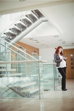 simsearch:6109-08953148,k - Pregnant businesswoman using mobile phone near stairs in office Stock Photo - Premium Royalty-Free, Code: 6109-08929335