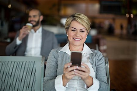 simsearch:6109-08802775,k - Smiling businesswoman using mobile phone in waiting area at airport terminal Photographie de stock - Premium Libres de Droits, Code: 6109-08929447
