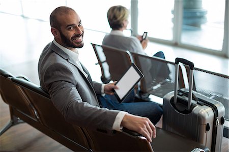 simsearch:6109-08929459,k - Portrait of smiling businessman with digital tablet sitting in waiting area at airport terminal Foto de stock - Royalty Free Premium, Número: 6109-08929450