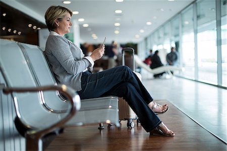 simsearch:6109-08929459,k - Businesswoman using mobile phone in waiting area at airport terminal Foto de stock - Royalty Free Premium, Número: 6109-08929451