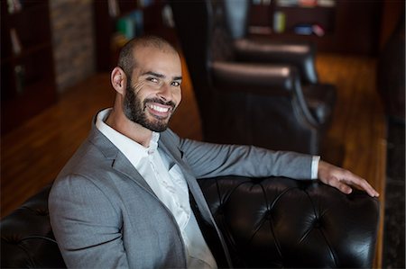 simsearch:6109-08929459,k - Portrait of smiling businessman sitting on sofa in waiting area at airport terminal Foto de stock - Royalty Free Premium, Número: 6109-08929454