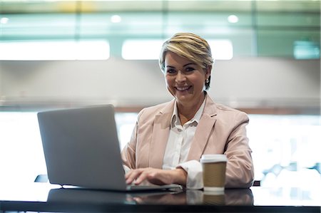 simsearch:6109-08929459,k - Portrait of smiling businesswoman using laptop in waiting area at airport terminal Foto de stock - Royalty Free Premium, Número: 6109-08929467