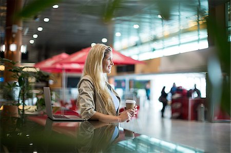 simsearch:6109-08700489,k - Smiling woman with coffee standing in waiting area at airport terminal Stock Photo - Premium Royalty-Free, Code: 6109-08929473