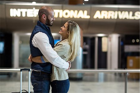 people hugging at airport - Cheerful couple embracing each other in waiting area at airport terminal Stock Photo - Premium Royalty-Free, Code: 6109-08929475