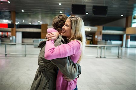 people hugging at airport - Cheerful couple embracing each other in waiting area at airport terminal Stock Photo - Premium Royalty-Free, Code: 6109-08929479