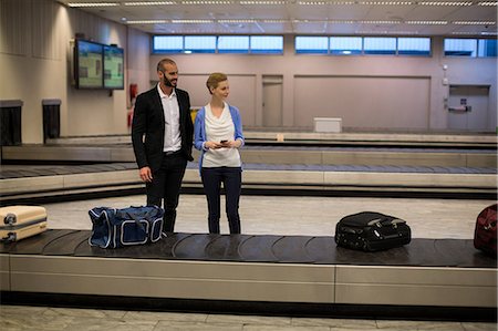 Couple waiting for luggage in baggage claim area at airport Stock Photo - Premium Royalty-Free, Code: 6109-08929491