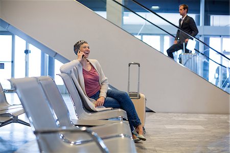 simsearch:6109-08802775,k - Smiling woman talking on mobile phone in waiting area at airport terminal Photographie de stock - Premium Libres de Droits, Code: 6109-08929497