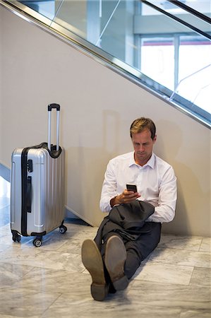 simsearch:6109-08722553,k - Businessman sitting on floor and using mobile phone in waiting area at airport terminal Foto de stock - Royalty Free Premium, Número: 6109-08929495
