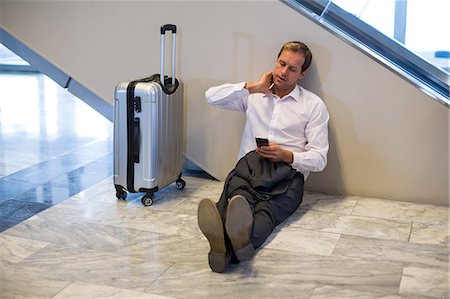 simsearch:6109-08929459,k - Businessman sitting on floor and using mobile phone in waiting area at airport terminal Foto de stock - Royalty Free Premium, Número: 6109-08929496