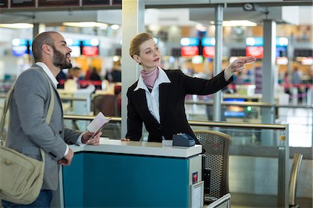 simsearch:6109-08929425,k - Airline check-in attendant showing direction to commuter at check-in counter in airport terminal Foto de stock - Sin royalties Premium, Código: 6109-08929409