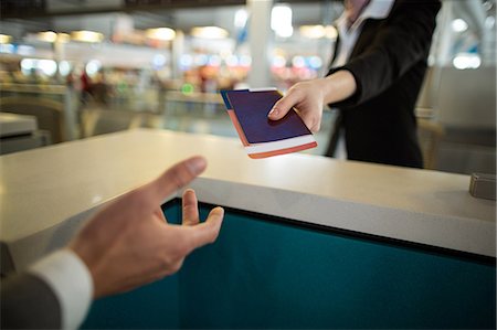 simsearch:6109-08929425,k - Airline check-in attendant giving passport to commuter at counter in airport terminal Foto de stock - Sin royalties Premium, Código: 6109-08929426