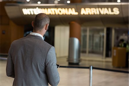 simsearch:6109-08929459,k - Rear view of businessman using digital tablet in waiting area at airport terminal Foto de stock - Royalty Free Premium, Número: 6109-08929433