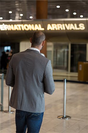 simsearch:6109-08929459,k - Rear view of businessman using digital tablet in waiting area at airport terminal Foto de stock - Royalty Free Premium, Número: 6109-08929434