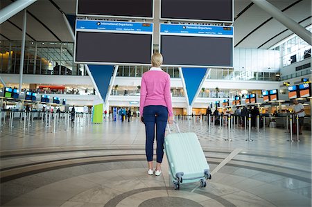 simsearch:6109-08929360,k - Rear view of female commuter standing with luggage at waiting area in airport Photographie de stock - Premium Libres de Droits, Code: 6109-08929566