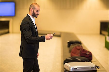 simsearch:6109-08944302,k - Businessman using mobile phone near baggage claim area at airport Stock Photo - Premium Royalty-Free, Code: 6109-08929569