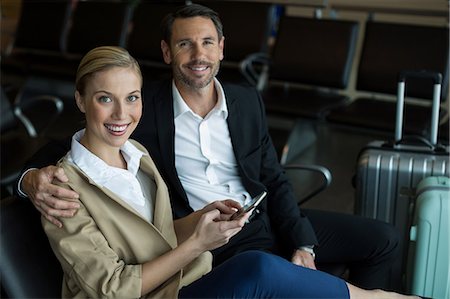 Portrait of happy couple using mobile phone at airport Stock Photo - Premium Royalty-Free, Code: 6109-08929586