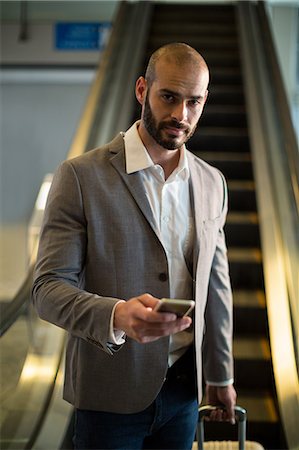 Portrait of businessman with luggage using mobile phone at airport Stock Photo - Premium Royalty-Free, Code: 6109-08929605