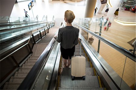 simsearch:6109-08929360,k - Rear view of businesswoman standing on escalator with luggage at airport Photographie de stock - Premium Libres de Droits, Code: 6109-08929620