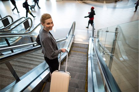 simsearch:6109-08929360,k - Businesswoman standing on escalator with luggage at airport Photographie de stock - Premium Libres de Droits, Code: 6109-08929622