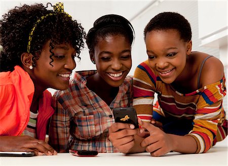 Three African teenage girls sitting indoors, looking at their cellphones Stock Photo - Premium Royalty-Free, Code: 6110-06702671