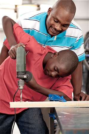 father and son workshop - African Father and son using a drill in a workshop Stock Photo - Premium Royalty-Free, Code: 6110-06702617